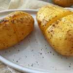 Two whole baked Potatoes with a cut in the middle topped with kosher salt and black pepper
