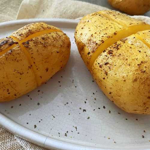 Two whole baked Potatoes with a cut in the middle topped with kosher salt and black pepper