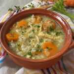Clear soup filled with shredded chicken, rice, sliced carrot and parsley