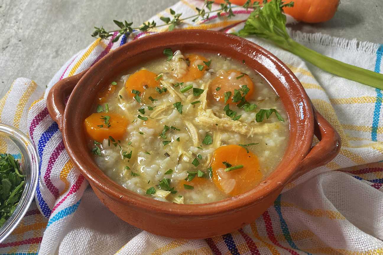 Clear soup filled with shredded chicken, rice, sliced ​​carrot and parsley