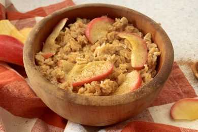 Rolled oats with cinnamon and red apples slices on top in brown bowl with apple slices on side