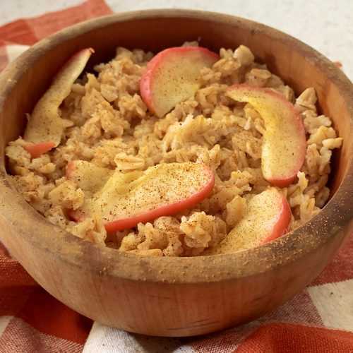 Rolled oats with cinnamon and red apples slices on top in brown bowl with apple slices on side