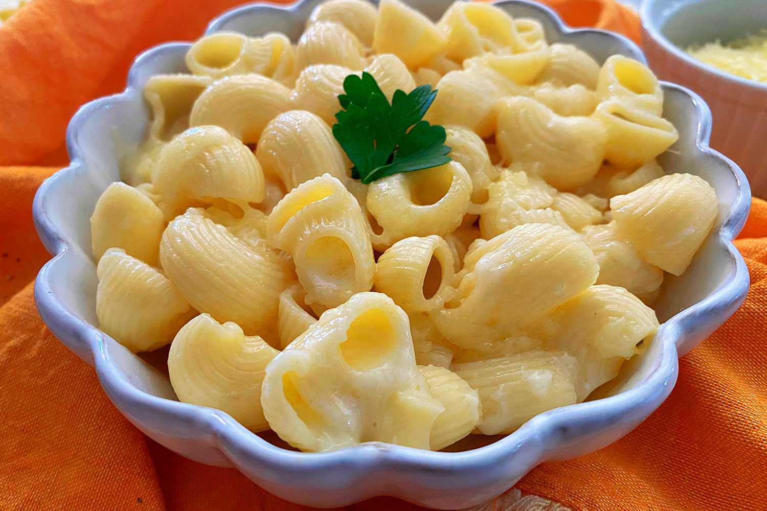 Macaroni mixed with melted cheese with parsley on top in white bowl