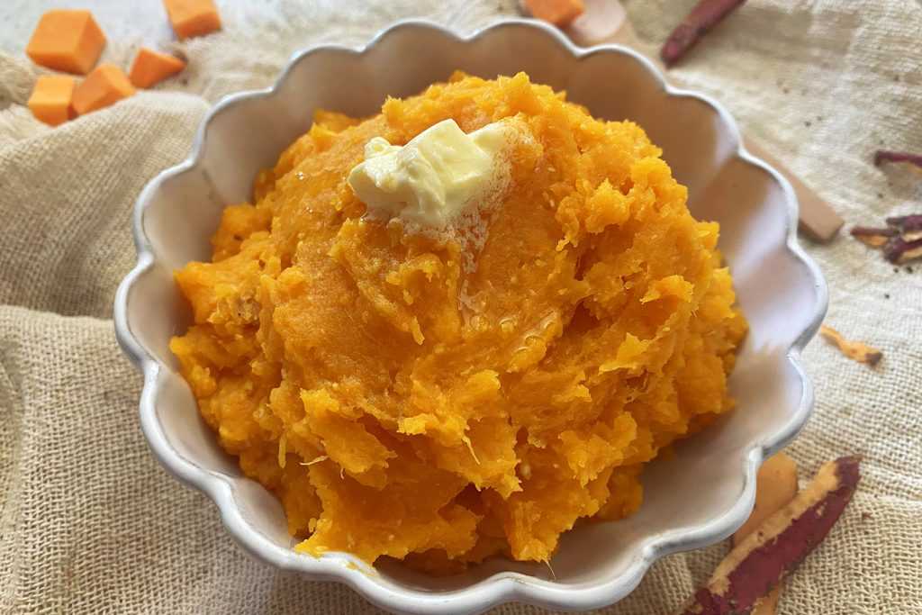 Mashed sweet potatoes in a white serving dish with butter melting on top.
