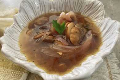 Clear soup with sliced mushrooms, red onions and parsley on top in white bowl