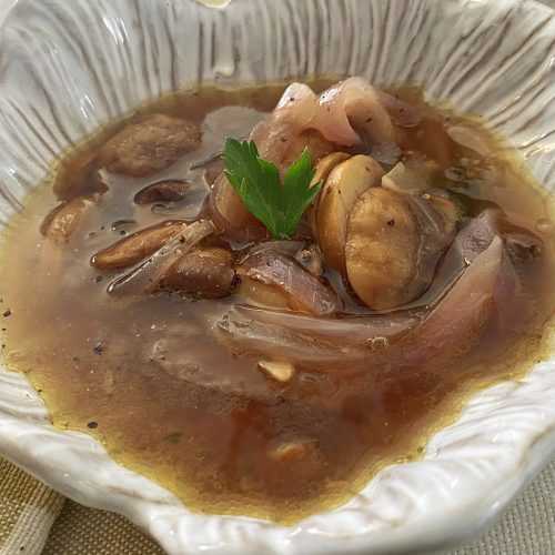 Clear soup with sliced mushrooms, red onions and parsley on top in white bowl
