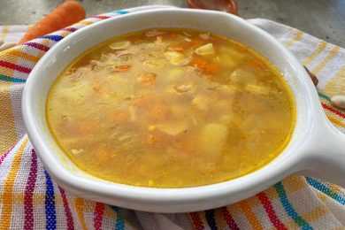 Clear soup with carrot and ham cubes, navy beans and chopped onion