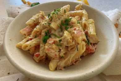 cooked penne pasta with chicken slices and bacon pieces in a cheesy sauce top with chopped parsley