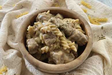 Fusilli pasta with beef cubes in a creamy sauce with oregano on top in brown bowl