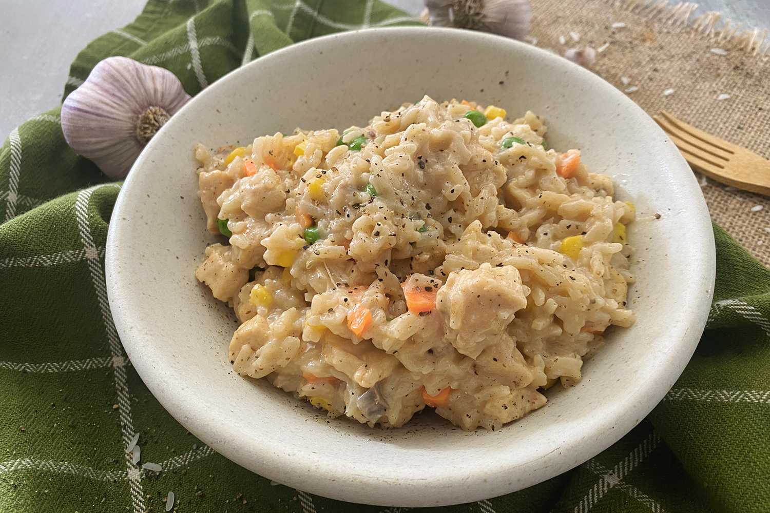 Cheesy mixture of rice, chicken cubes, carrot, corn and peas in white bowl.