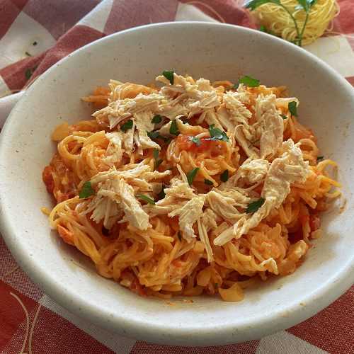 Spaghetti in red sauce with chopped onion, shredded chicken and chopped parsley on top in white bowl