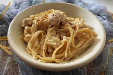 Fettuccine in heavy cream sauce mixed with chicken cubes on white bowl