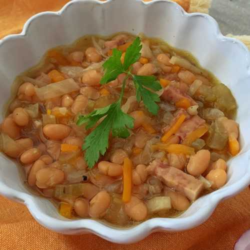 Soup bowl filled with cabbage, carrot, onion, garlic, beans and ham and topped with fresh parsley