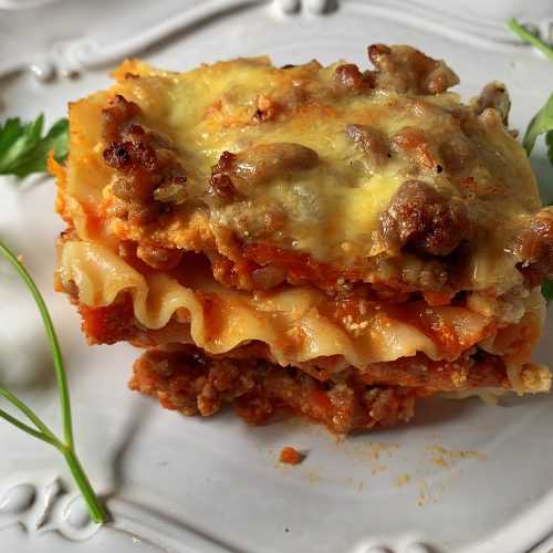 Lasagna slice with ground beef and tomato sauce topped with melted cheese with parsley on side