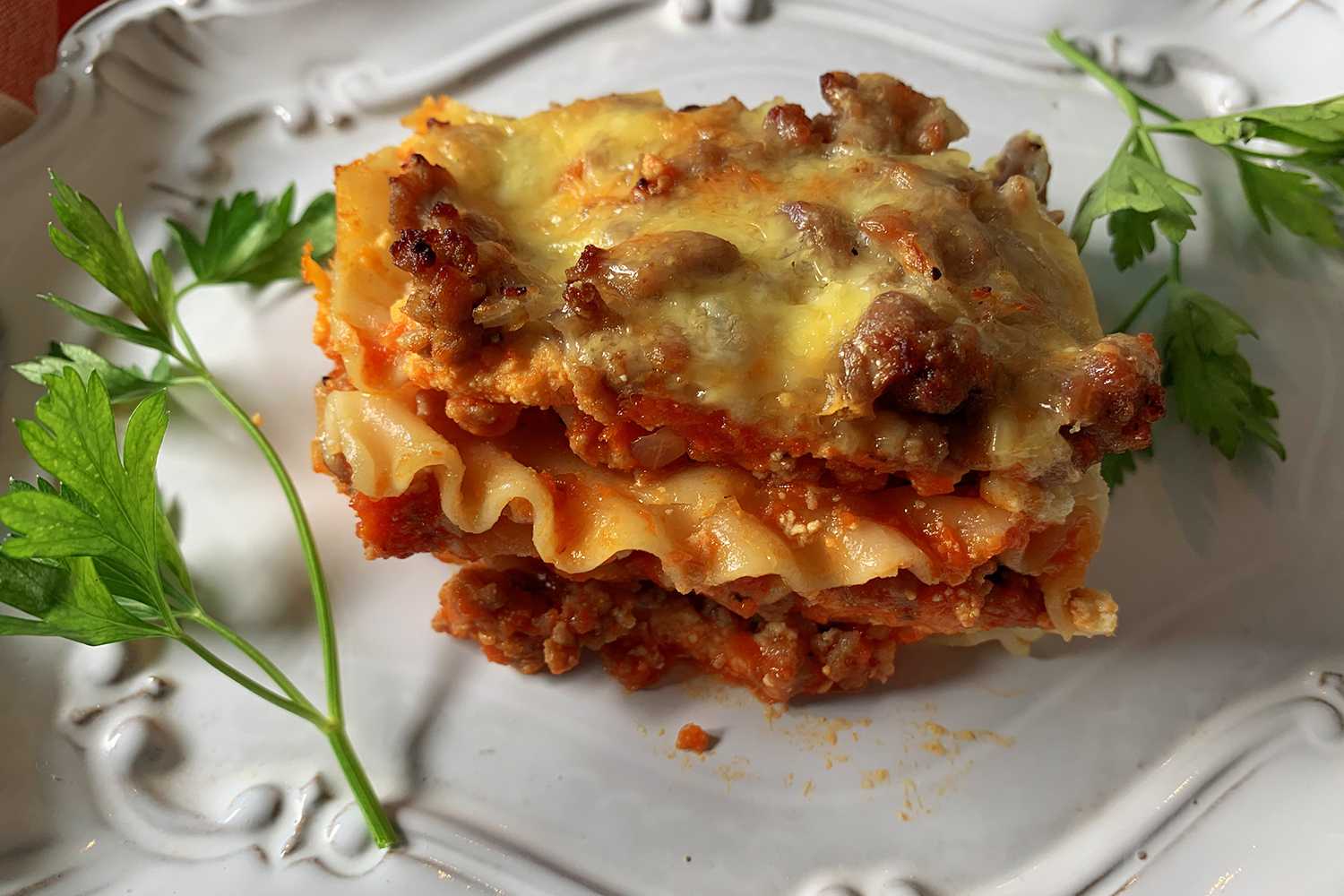 Lasagna slice with ground beef and tomato sauce, topped with melted cheese with parsley on side