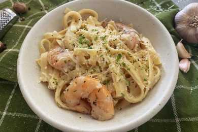 Fettuccine mixed with shrimp with shredded cheese and black pepper on top in white bowl