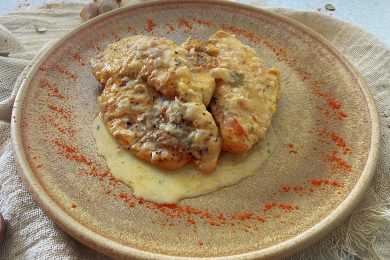 Two chicken fillets with creamy sauce on top and paprika on side in brown plate