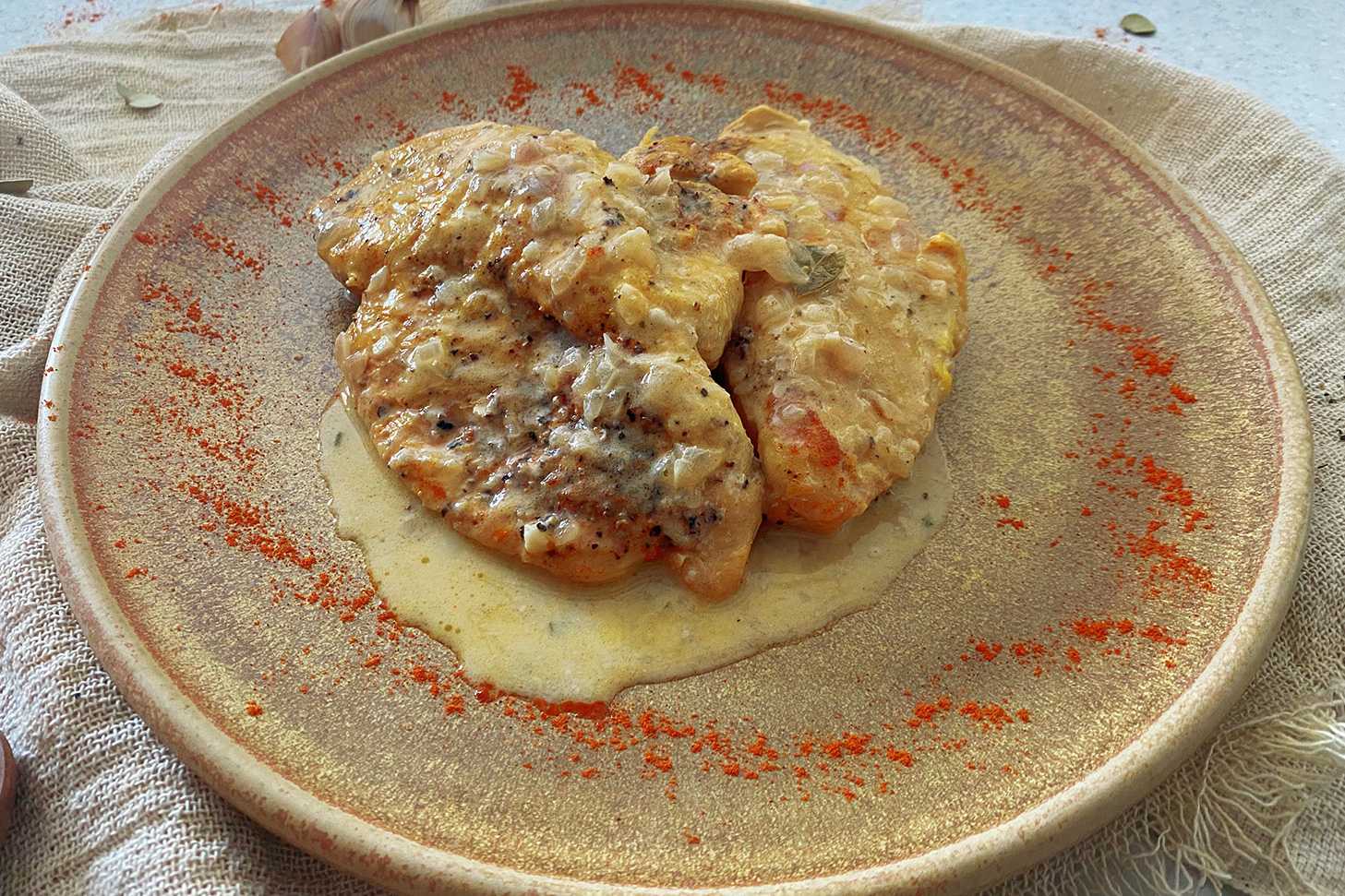 Three chicken fillets with creamy sauce on top and paprika on side in brown plate