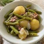 Green beans with boiled potatoes, onion slices and chopped bacon in white bowl