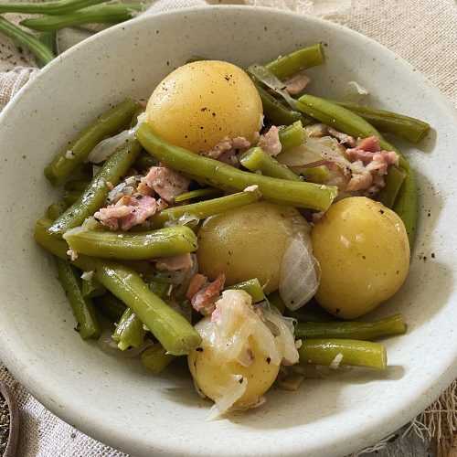 Green beans with boiled potatoes, onion slices and chopped bacon in white bowl