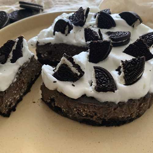 Cheesecake with chocolate crust on bottom and whipped cream with crushed Oreo cookies on top with one slice cut out