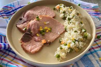 Cooked rice mixed with corn and peas with pork chops on side on a plate