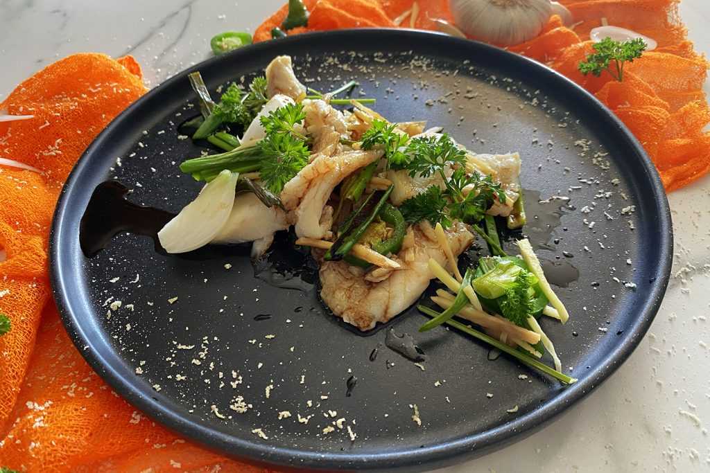 seabass pieces with spring onion, onion, coriander leaves on a black plate