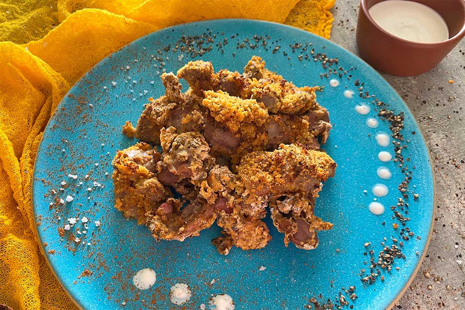 Cooked chicken gizzards coated with bread crumbs on a blue plate with ground pepper
