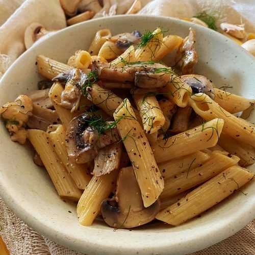 Penna pasta with chicken cubes and mushroom slices on a white bowl
