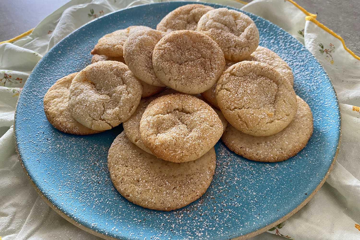 Batch of sugar cookies on a blue plate topped with sugar powder