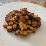Crispy tofu cubes on each other on a white plate with garlic powder on side