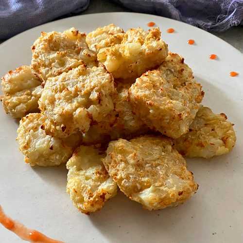 Homemade cauliflower tots on a white plate decorated with orange sauce