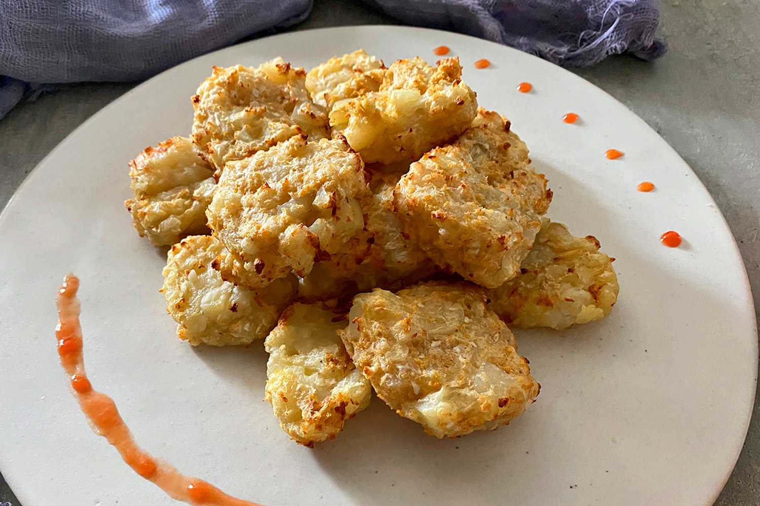 Homemade cauliflower tots on a white plate decorated with orange sauce