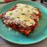 Five Enchiladas laying next to each other topped with bbq sauce and melted cheese with parsley