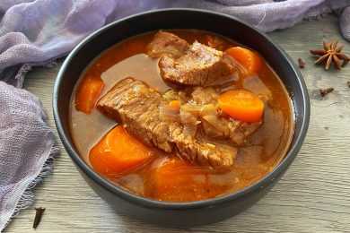 Clear soup with beef steak, carrot cubes and chopped onion in a black bowl
