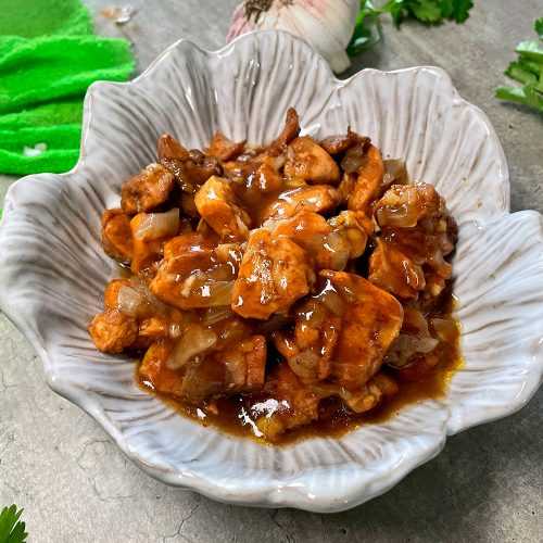 Chicken cubes in a brown sauce with chopped onions in a white bowl