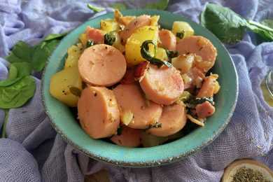 Sausage slices with potato cubes and spices in a blue bowl top view