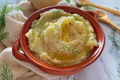 Mashed potatoes topped with ground pepper and leaves in a brown bowl with wooden spoons on side