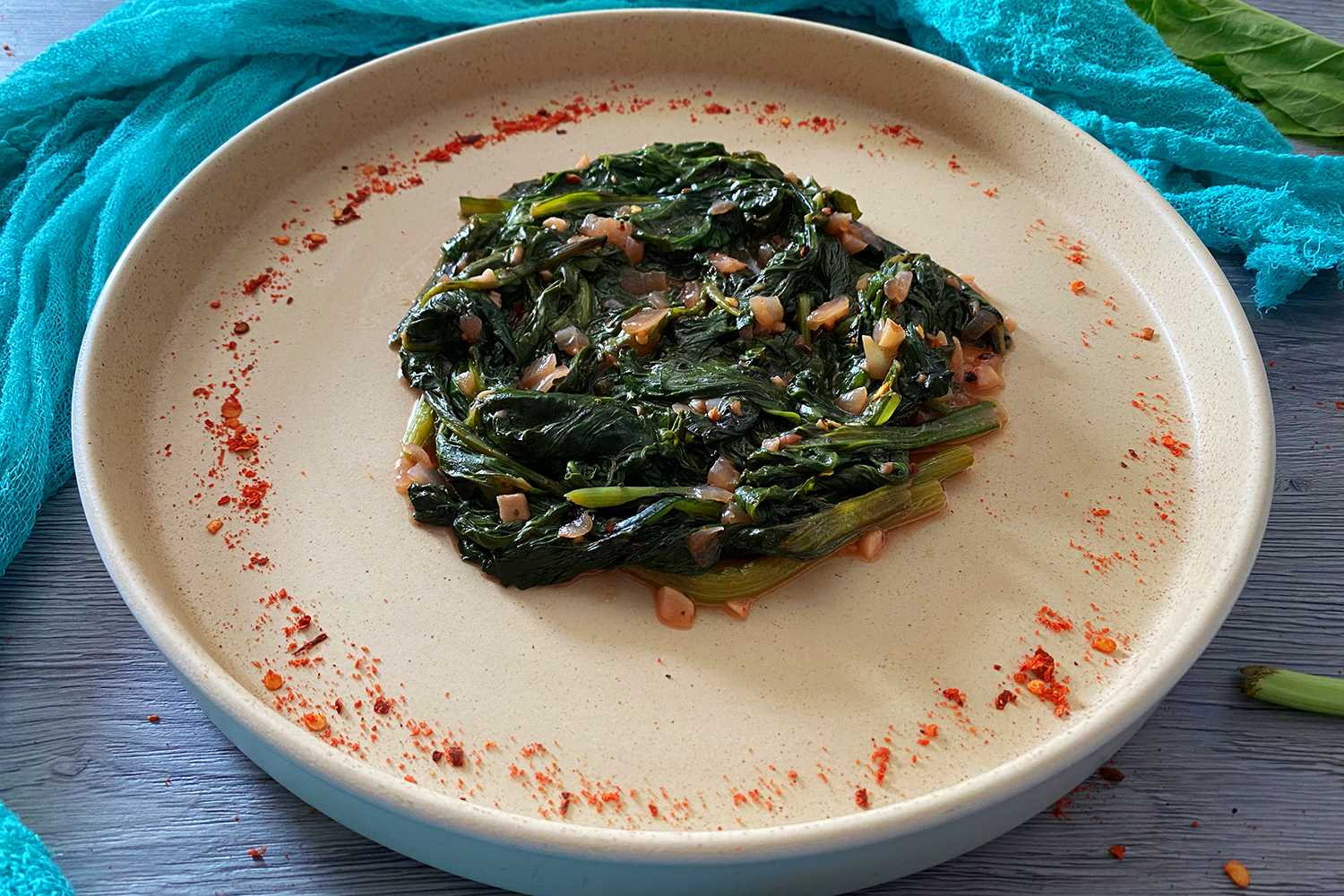 Cooked Collard topped with minced garlic and onion on a gray plate top view