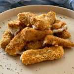 Crispy sticks coated with bread crumbs filled with melted cheese on white plate