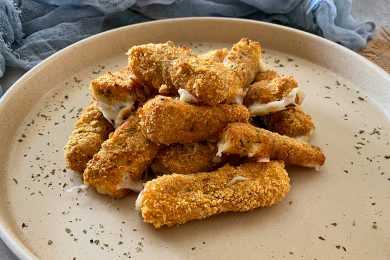 Crispy sticks coated with bread crumbs filled with melted cheese on white plate