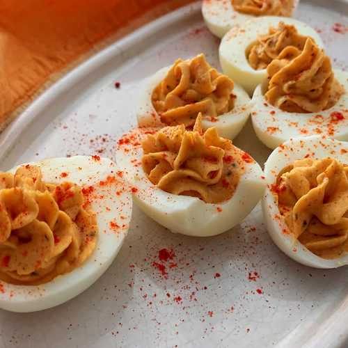 Hard boiled eggs cut into half filled with egg and mustard mixture and topped with paprika