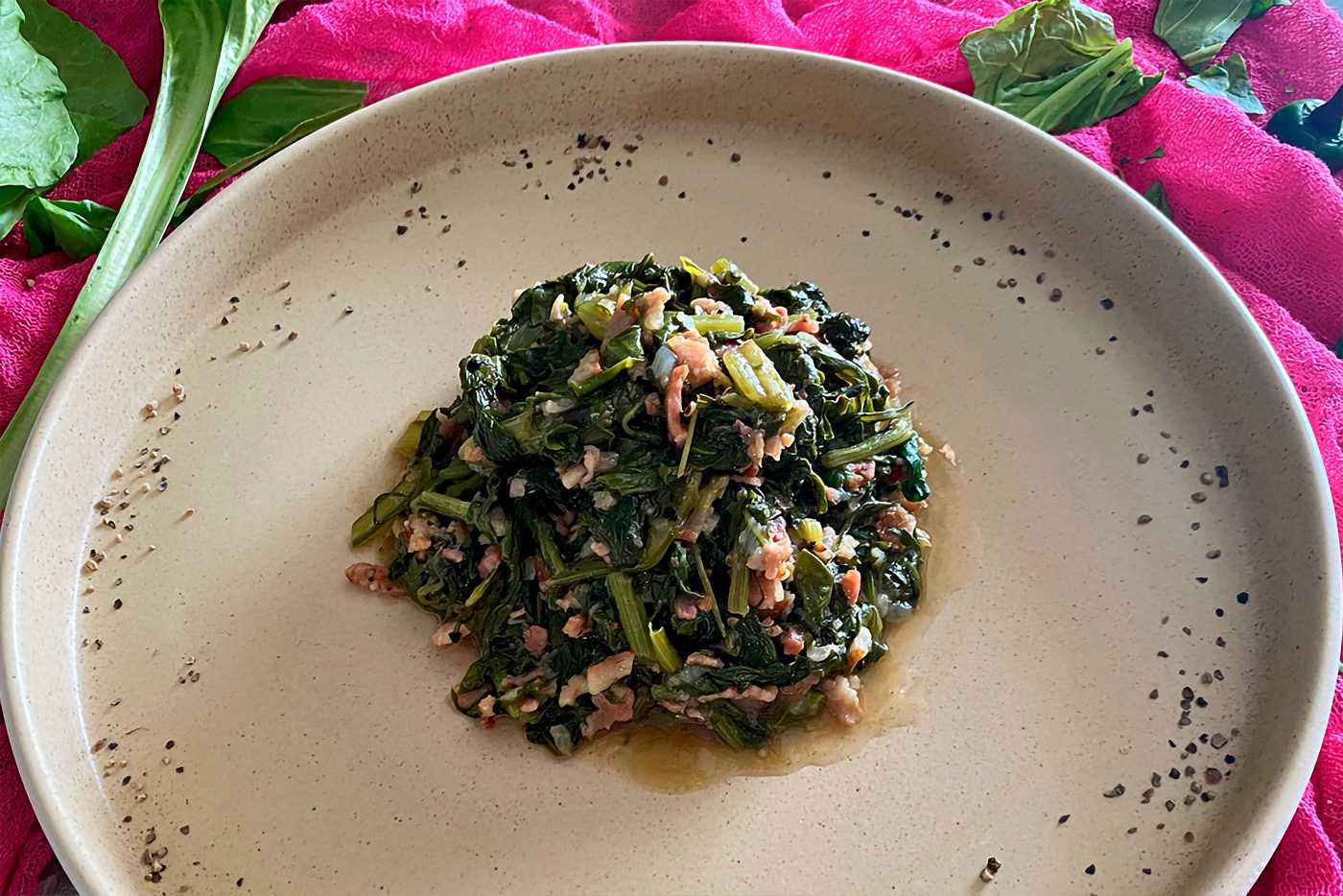 Small serving of collard greens with bacon on a white plate.