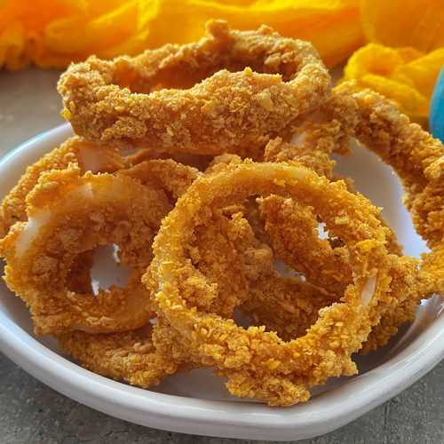 Homemade onion rings coated with bread crumbs on a white bowl