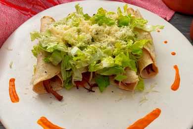 Four taquitos filled with beef topped with shredded lettuce and melted cheese