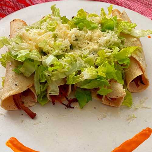 Four taquitos filled with beef topped with shredded lettuce and melted cheese
