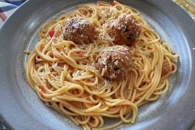 Cooked spaghetti noodles with tomato sauce topped with cheese and meatballs