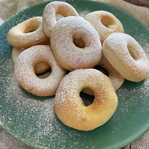 Small homemade donuts on each other with sugar powder on top and on the plate
