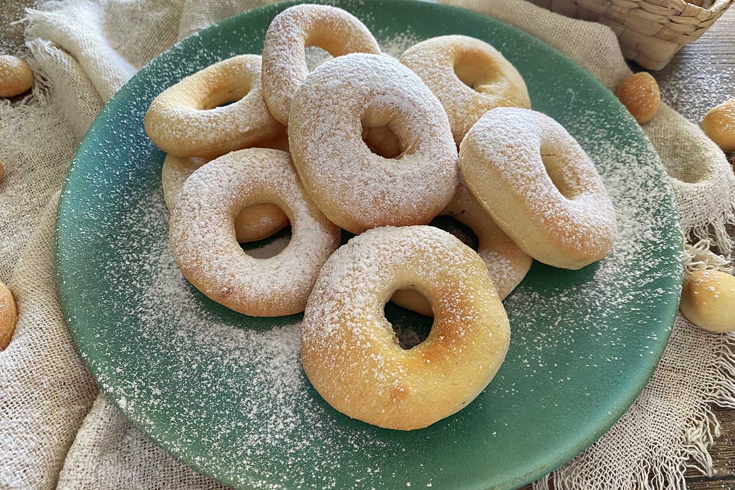 Small homemade donuts on each other with sugar powder on top and on the plate