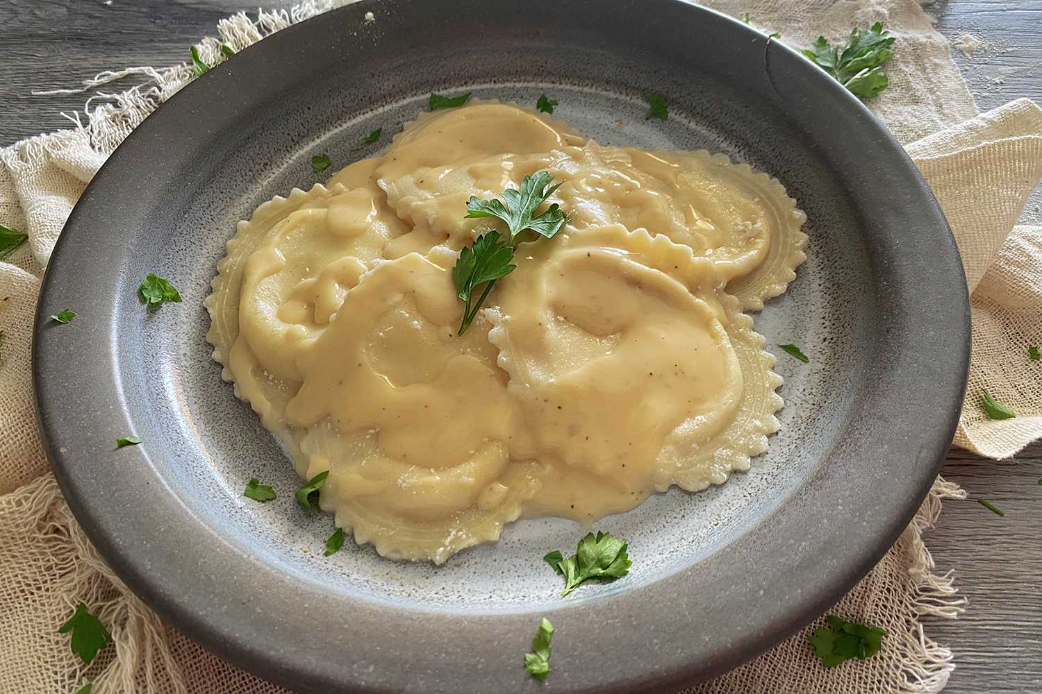 Ravioli in a gray plate with alfredo sauce and parsley on top